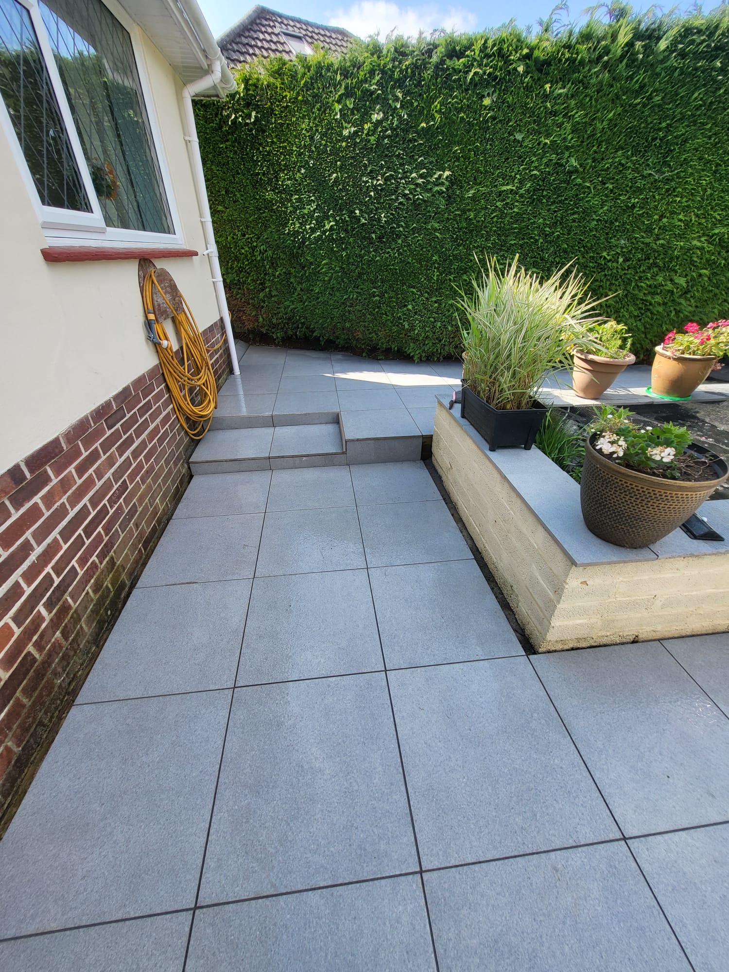 Grey tiled patio beside a neatly trimmed hedge